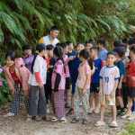 Grupo de crianças participa de uma atividade educativa em uma trilha natural, acompanhado por dois adultos.