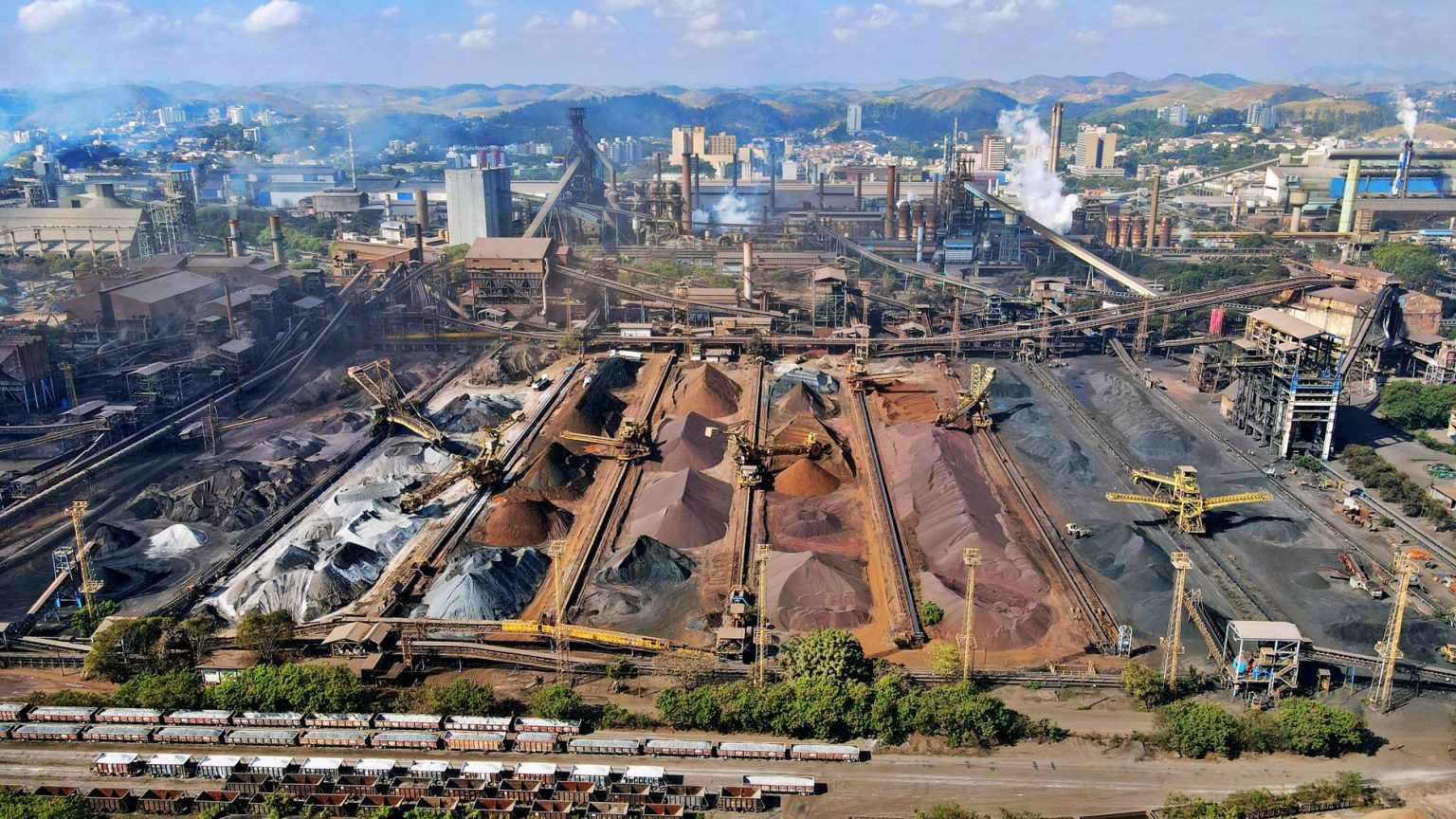 Vista ampla de uma instalação industrial de mineração, com máquinas e pilhas de rejeitos.