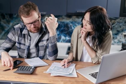 Casal analisa contas e documentos financeiros diante de um laptop em casa.
