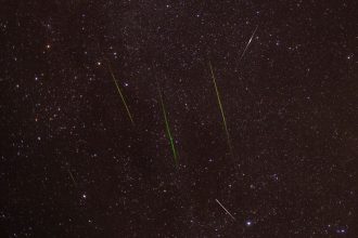 Meteoros traçam riscos luminosos no céu noturno estrelado.