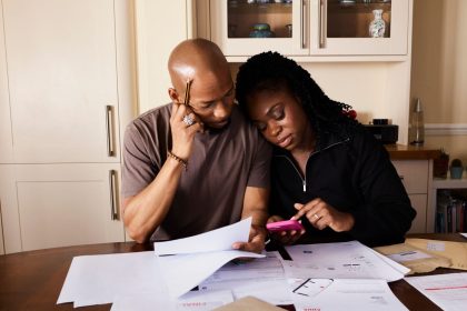 Casal consulta documentos e usa um celular enquanto organiza as finanças domésticas à mesa.