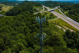 Torre de comunicação entre áreas verdes, ao lado de uma rodovia com veículos.