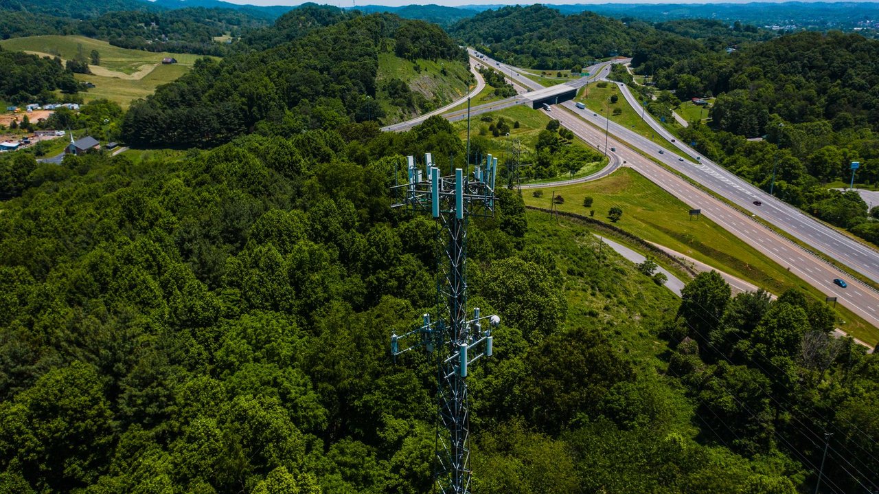 Torre de comunicação entre áreas verdes, ao lado de uma rodovia com veículos.