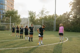 Jogadoras de futebol feminino realizam exercícios em campo ao ar livre enquanto uma treinadora ou treinador observa.
